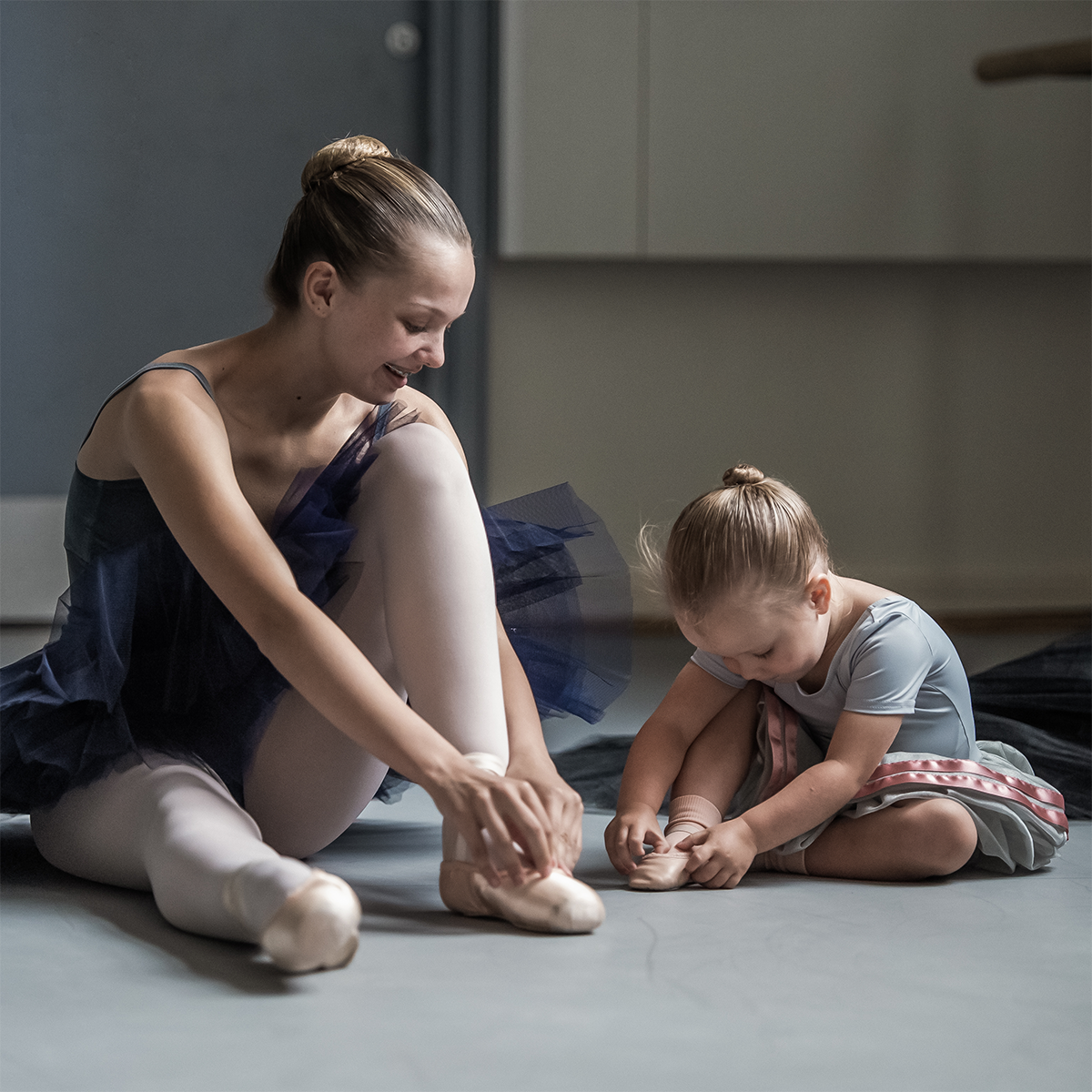 Two young ballet dancers wearing their bbodance uniform putting on their ballet shoes