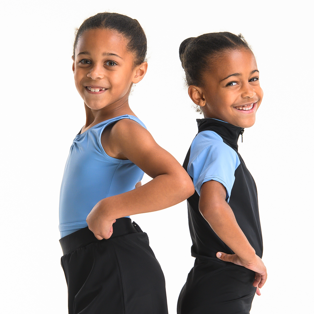 Two young female dancers posed back to back wearing ISTD blue leotards and black shorts on a white background